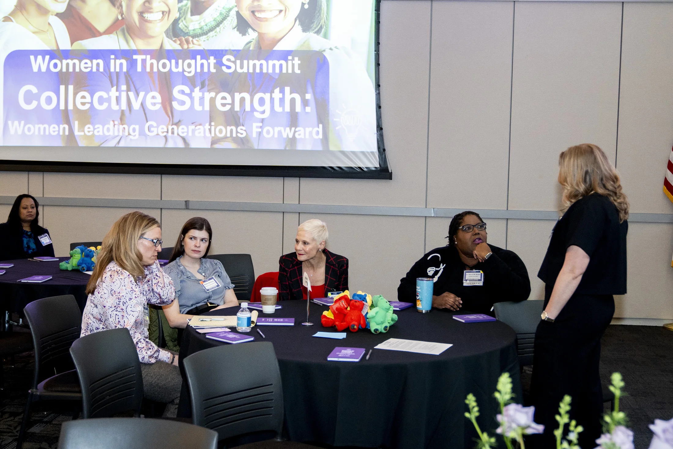 Women participating in a facilitated Women in Thought Summit session with the event identity, tables, materials, and presentation environment visible.