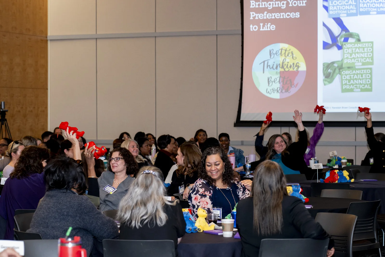 Women in Thought Summit participants raising materials during a facilitated table activity with presentation content visible in the room.